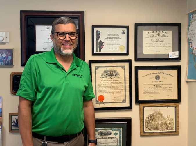 Shane Mudge next to a wall of his family’s railroading awards and achievements. 